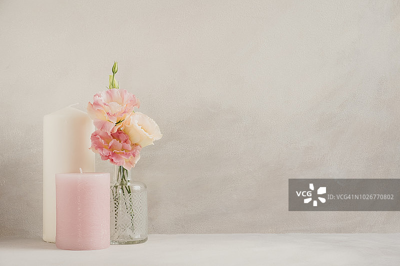 粉彩风格的粉色/奶油色丽西斯，在小玻璃花瓶中，以及两支蜡烛，背景是水彩效果的灰色库存图片图片素材