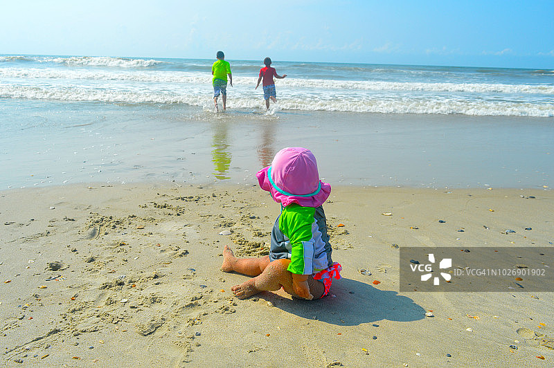 10个月大的女婴看着两个朝大海跑去的男孩图片素材