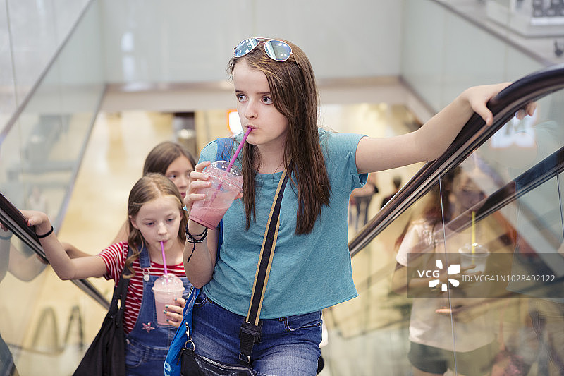 三名女孩在购物中心乘坐自动扶梯，同时喝着冰沙图片素材