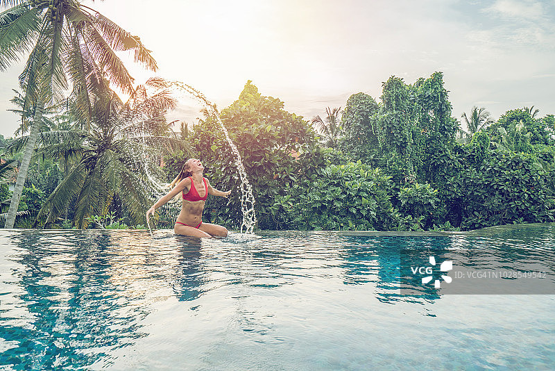 年轻女子在巴厘岛无边泳池中甩头发，享受度假乐趣图片素材