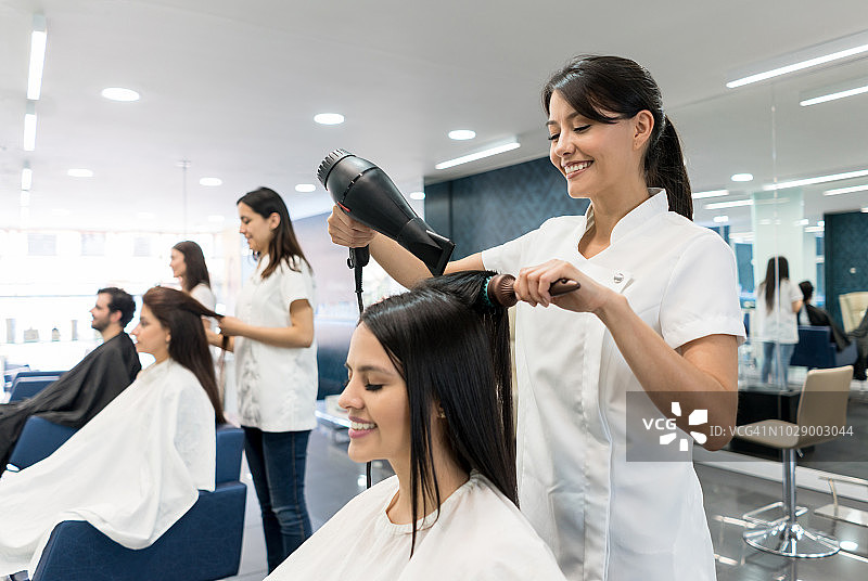 美丽的拉丁美洲发型师为女顾客吹发，两人都很开心图片素材