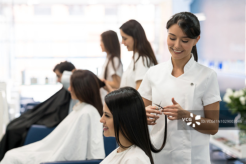 年轻女造型师在沙龙为顾客剪发图片素材