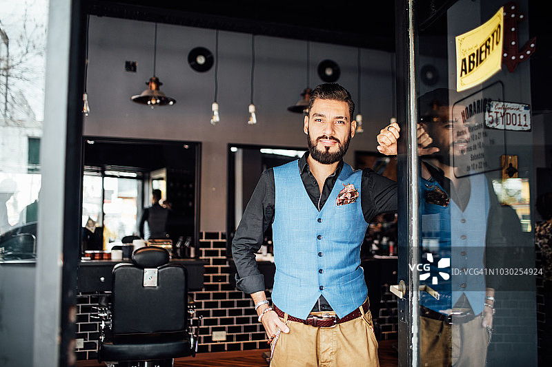 自信的理发师站在商店入口图片素材