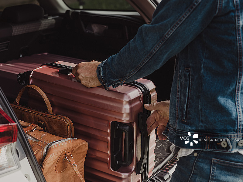 男子将行李箱装入车内，准备自驾游图片素材