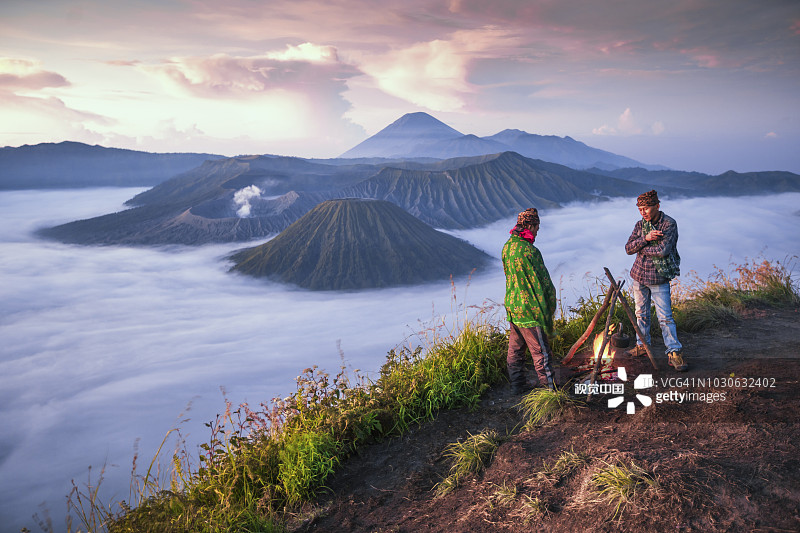 日出时分，两名印度尼西亚当地人在布罗莫火山背景下篝火图片素材
