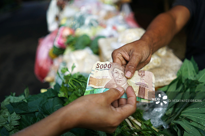 顾客将印尼盾纸币递给蔬菜供应商图片素材