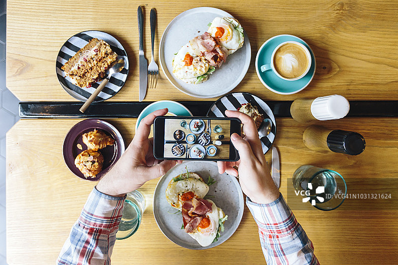 个人视角：男人在咖啡馆用手机拍早午餐图片素材