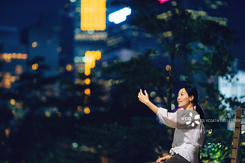 微笑女人在城市公园夜晚用智能手机建立视频会议图片素材