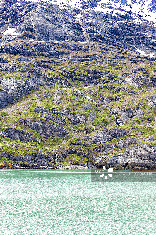 从游轮航行在内湾航道上看到的，从崎岖的雪山流向美国阿拉斯加冰川湾约翰霍普金斯海湾的溪流图片素材