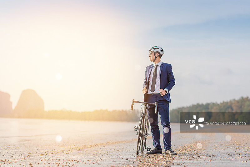 年轻的亚洲商务男人在日落时于海滩骑自行车放松身心图片素材