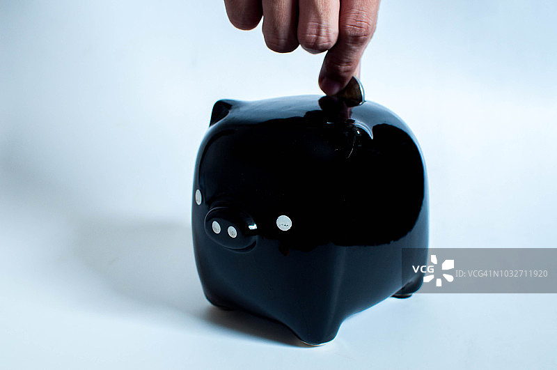 往黑色小猪存钱罐里投币图片素材
