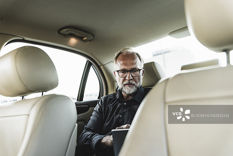 年长的商人坐在汽车后座上，使用平板电脑图片素材