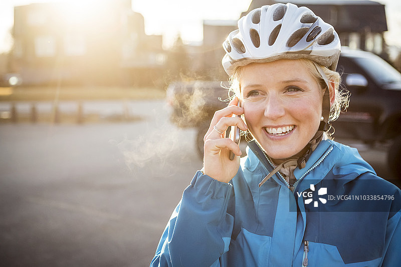阳光下，戴自行车头盔的年轻女子正在用手机通话图片素材