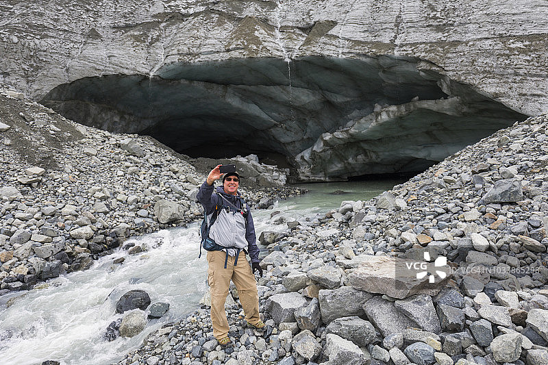 男性徒步旅行者在古尔卡纳冰川冰洞前用手机自拍图片素材
