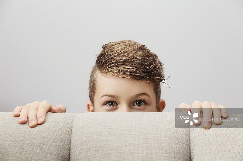 从沙发后面探头看镜头的小男孩肖像图片素材