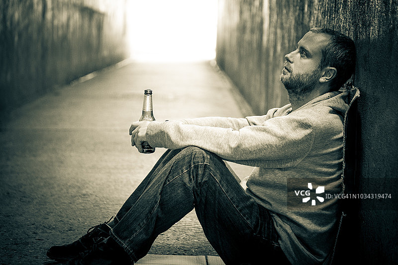 坐在黑暗地铁隧道里，用玻璃瓶喝啤酒的年轻白人男子图片素材
