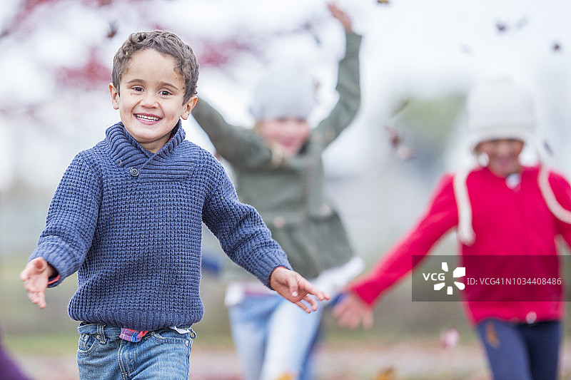 可爱的男孩和朋友们在落叶中奔跑图片素材