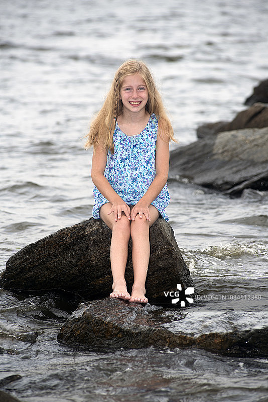 坐在岩石防波堤上的十岁女孩图片素材