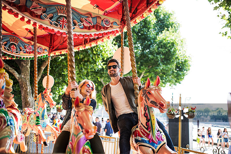 一对戴着太阳镜的年轻夫妇快乐地骑在旋转木马上图片素材