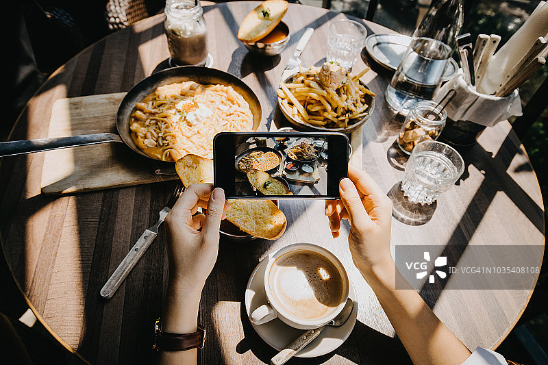 在餐厅里，女人用智能手机拍摄与朋友们愉快用餐的快照图片素材