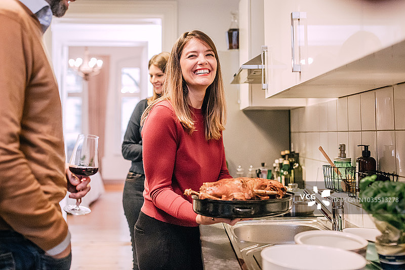 年轻女人在厨房里笑着拿着圣诞家禽图片素材