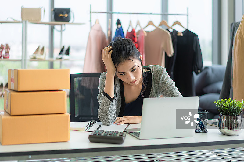 创业失败的亚洲小企业主在工作场所感到沮丧。亚洲自由职业女性卖家检查产品订单，准备发货给客户。在线销售业务失败。图片素材