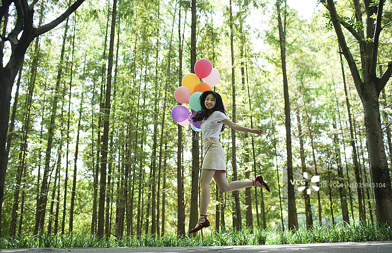 快乐的亚洲女性手持彩色气球奔跑，森林背景图片素材
