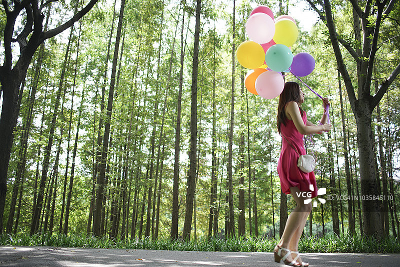 快乐的亚洲女性手持彩色气球奔跑，森林背景图片素材