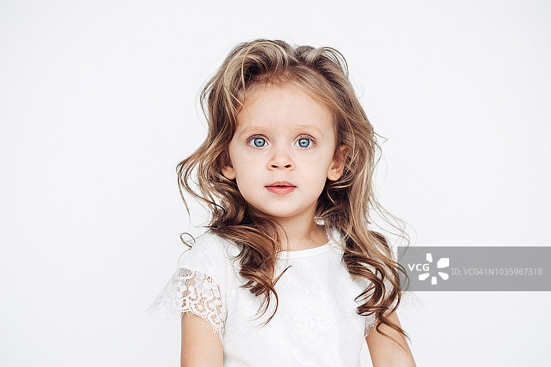 穿着白色连衣裙对着镜头微笑的可爱小女孩图片素材