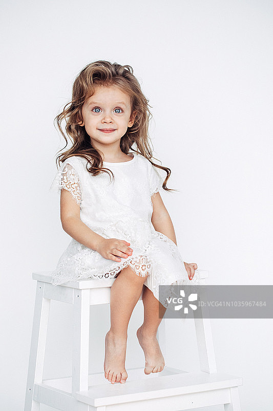穿着白色连衣裙对着镜头微笑的可爱小女孩图片素材