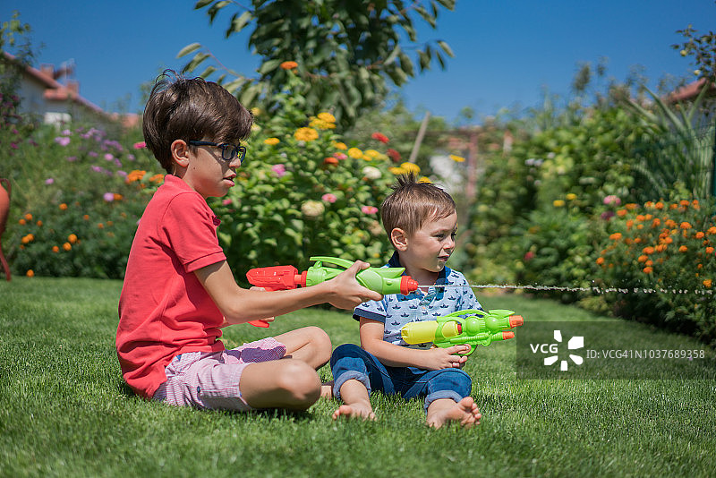 快乐的兄弟在草地上玩水枪图片素材