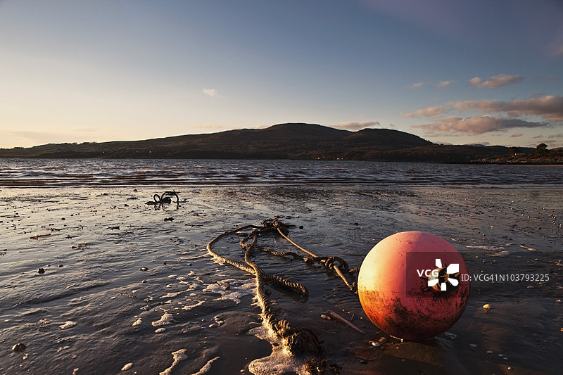 一根绳子系在潮汐中躺在海岸上的浮标上图片素材