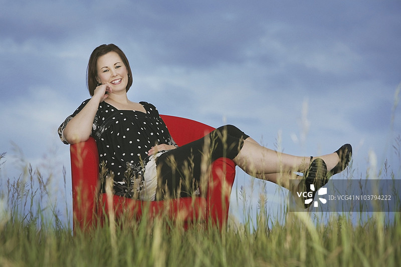 一位女性坐在田野中央的红色椅子上图片素材