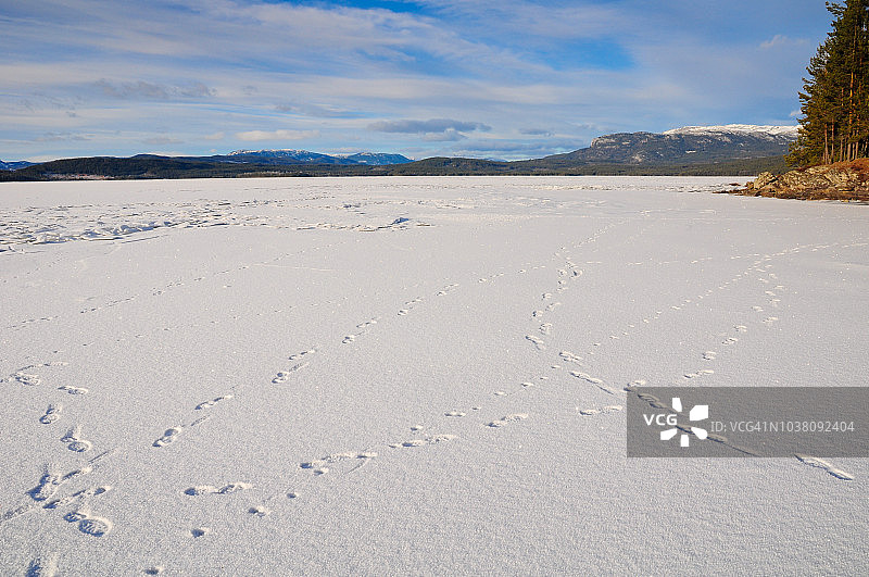 冬季冰冻湖面上的脚印和远处雪山图片素材