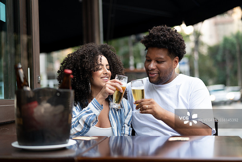 快乐的年轻夫妇在酒吧里用啤酒祝酒图片素材