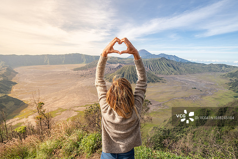 年轻女子在火山景观的山顶上用手指比心，眺望布罗莫火山 - 人们热爱旅行冒险图片素材