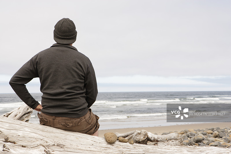 男子坐在海边浮木上图片素材
