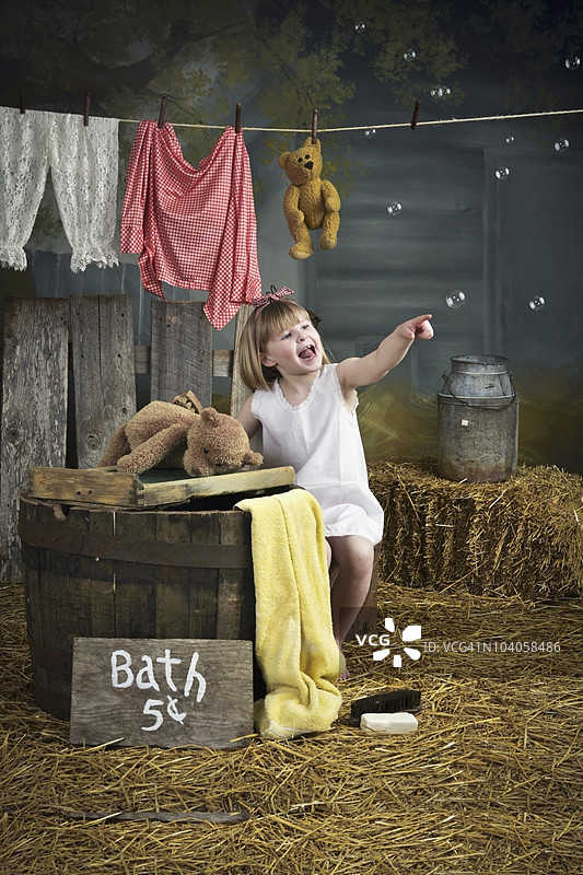 女孩指着泡泡，站在带有沐浴标志的桶旁边图片素材