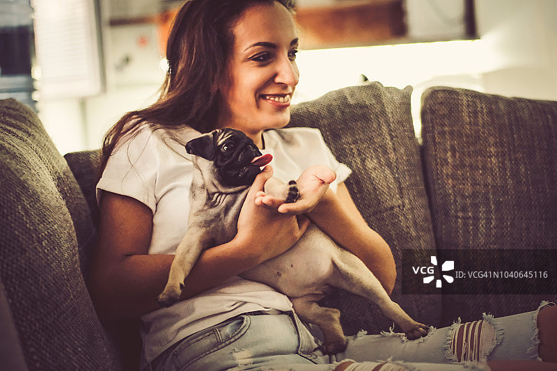 在客厅里和巴哥犬坐在一起的年轻女人图片素材