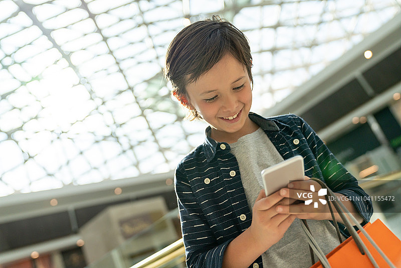 快乐的男孩在购物中心购物并用手机发短信图片素材