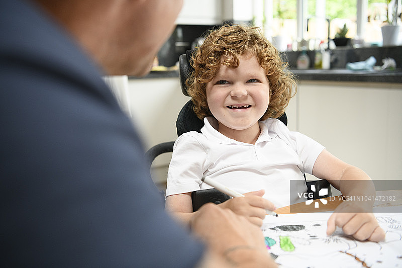 坐在轮椅上在餐厅里画画的快乐男孩图片素材