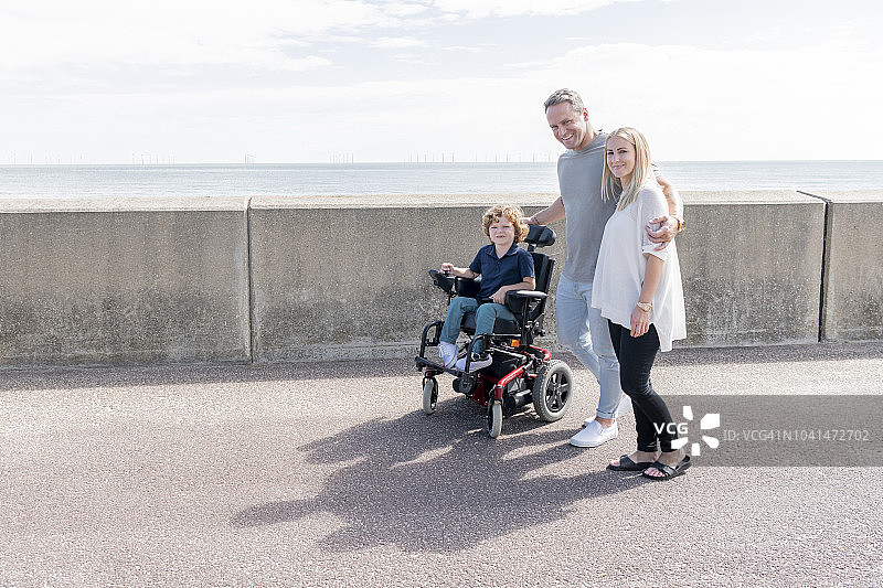 男孩坐在轮椅上，父母在海边陪伴图片素材