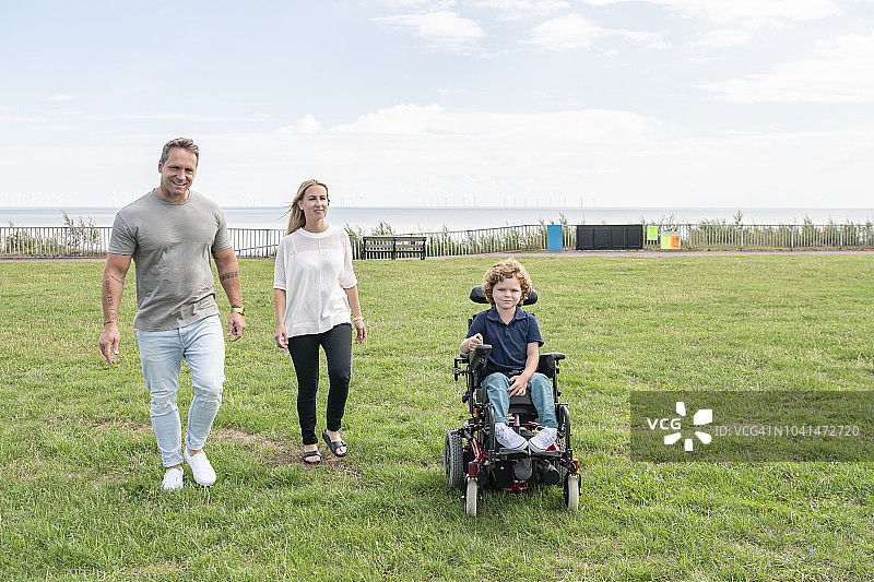 残疾男孩在父母的陪伴下操控轮椅在草地上行驶图片素材