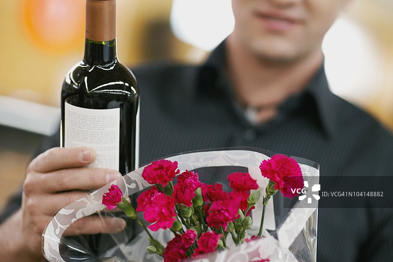 一名男子手持一瓶葡萄酒和一束花的中景视图图片素材
