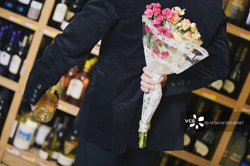 男子手捧鲜花和葡萄酒瓶的腰部特写图片素材