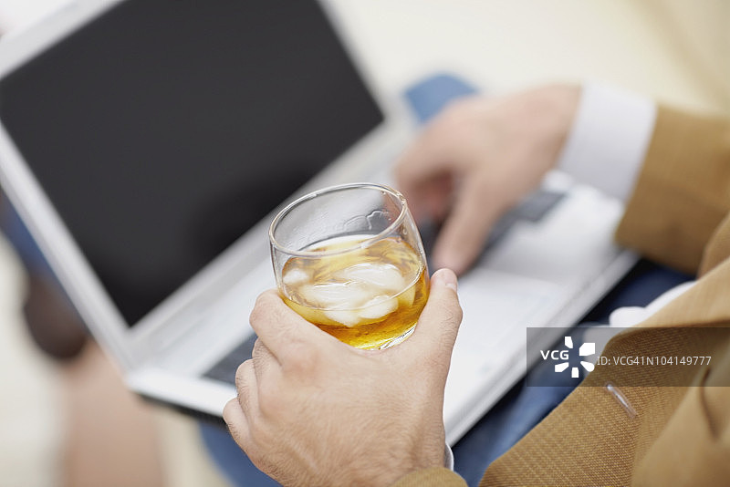 男人用笔记本电脑并拿着一杯葡萄酒的半身视角图片素材