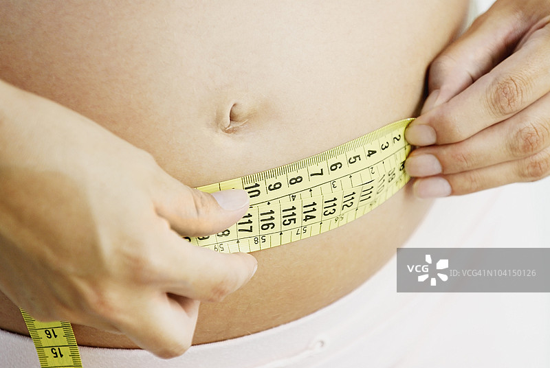 孕妇用卷尺测量腹部的中部视图图片素材