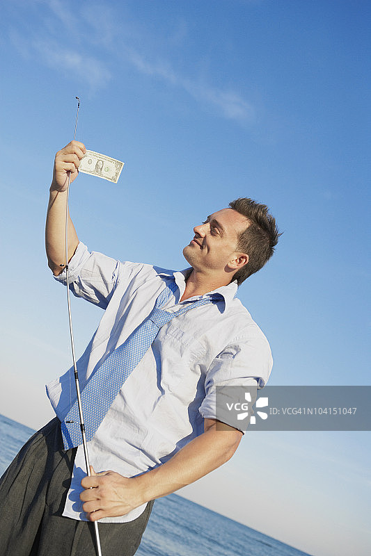 手持钓鱼竿和美元钞票的年轻男人图片素材
