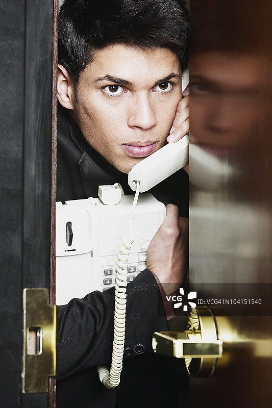 商人使用电话并从门后偷看的特写镜头图片素材