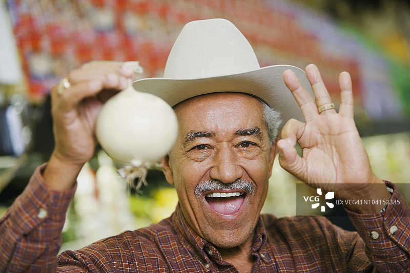 拿着白色洋葱并做出OK手势的年长男人肖像图片素材